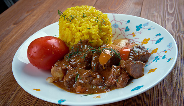 A plate of Seco, an Ecuadorian meta stew served with yellow rice and a tomato A plate of Seco, an Ecuadorian meta stew served with yellow rice and a tomato