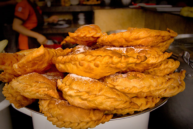 A tray of Empanadas de viento with a person cooking in the background A tray of Empanadas de viento with a person cooking in the background