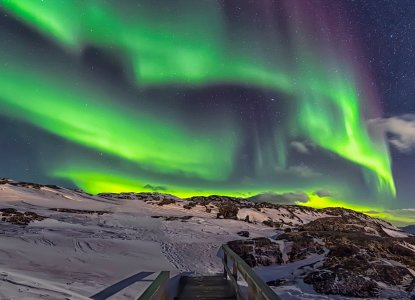 Snow and rocky covered  in the dark with bright green Northern Lights (Aurora Borealis)  in the sky in Illulissat Greenland) 
