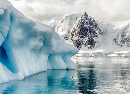 interesting blue iceberg formation in calm Antarctic waters in Polar Circle with snowy mountains in background) 